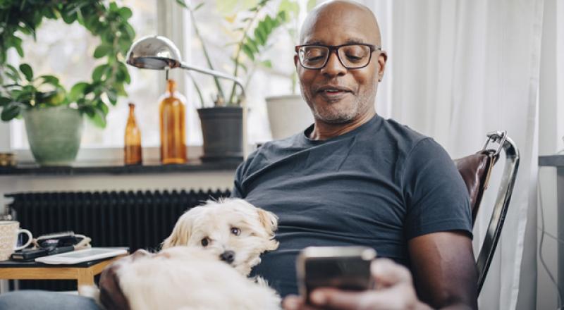 Man looking at a smartphone with a dog on his lap