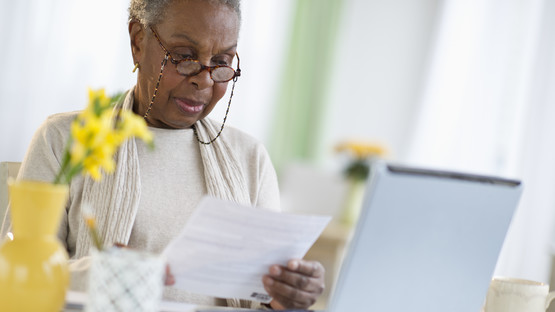 Elderly woman reading a letter in front of a laptop - Frequently Asked Questions