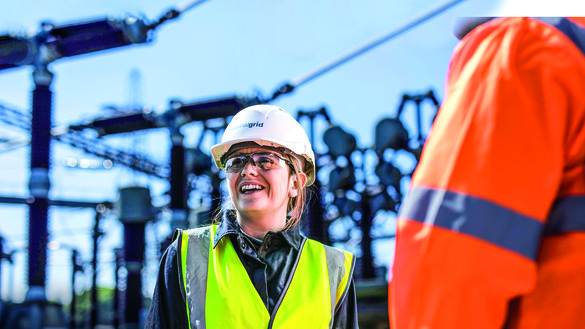 National Grid worker with an out of focus industrial site in the background under a blue sky 