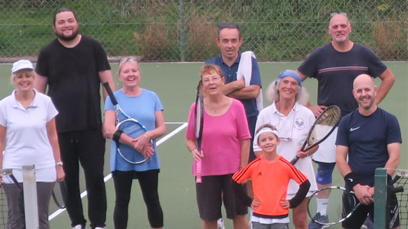 Group of people, some holding tennis rackets, on a tennis court