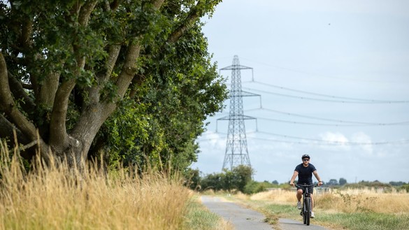 Man wearing t-shirt, shorts and a helmet cycling along a country lane with a pylon in the background