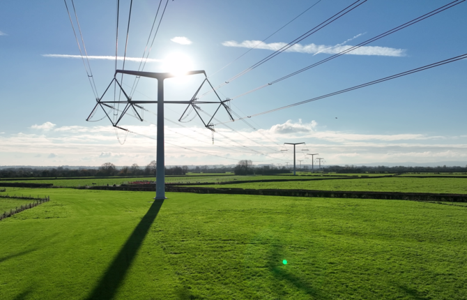 T-pylons and overhead electricity lines in the sunshine in green fields