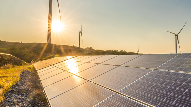 Solar panels and wind turbines in a field with the sun shining behind