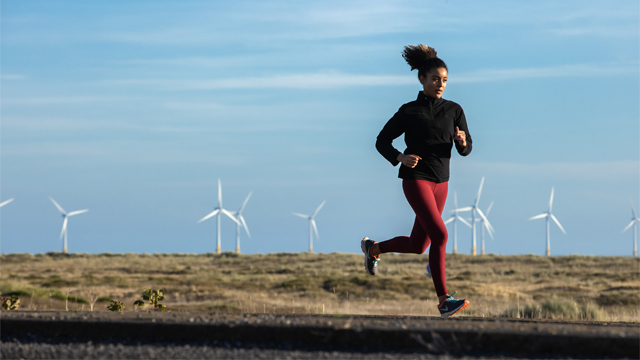 Woman running along a beach with wind turbines in the background