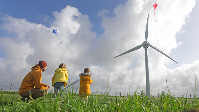 Man and two children playing with kites in field with wind turbines