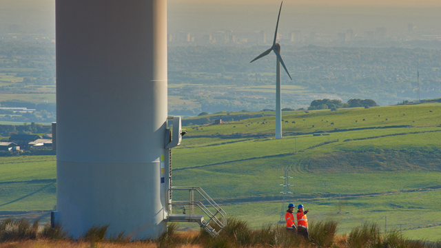 Two windfarm engineers wearing orange high-vis jackets at the foot of a wind turbine