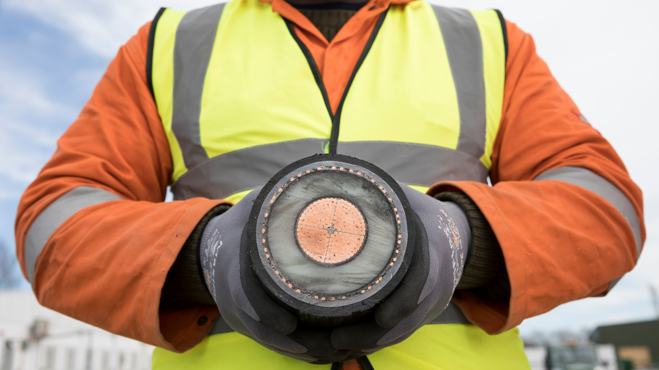 Close up of a person wearing orange overall and high-vis vest holding a section of an interconnector cable