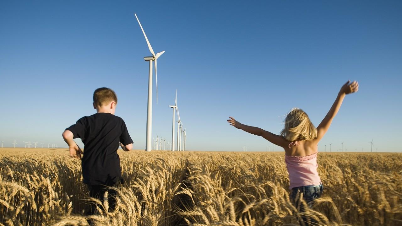Children running through a corn field with wind turbines