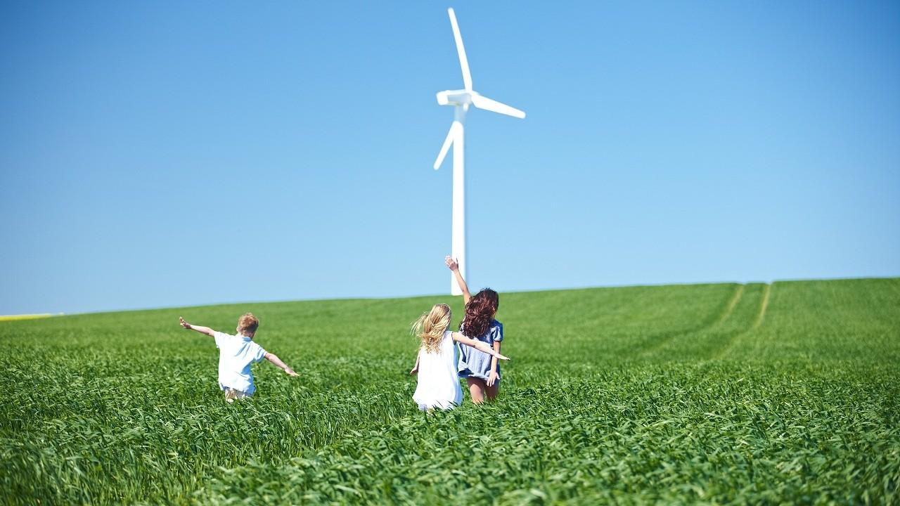 Children running through a green field with a wind turbine