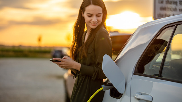 Person holding a mobile device leaning against electric vehicle while it's charging