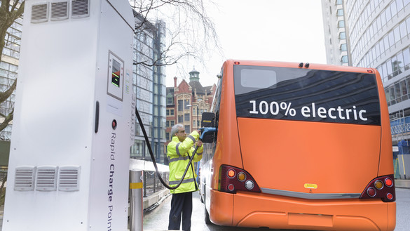 An orange electricity bus being connected to a fuel point by a man