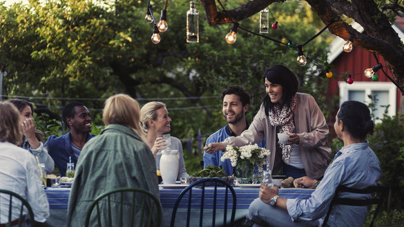Group of people having dinner in a garden under a tree with a string of lights in it