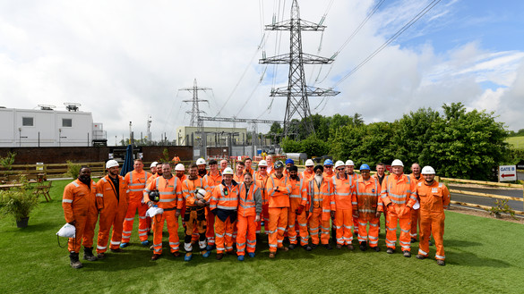 National Grid's construction health hub team wearing orange overalls in a green field with pylons in the background