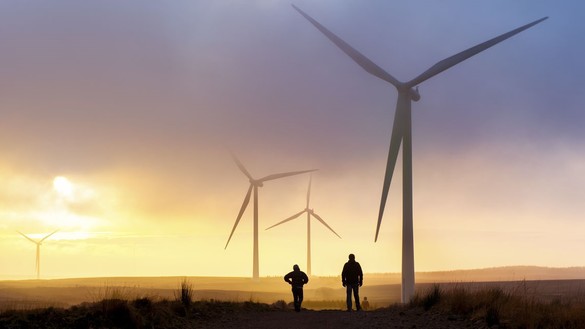 Two people standing under a wind turbine at sunset for National Grid article