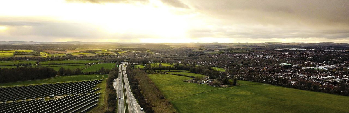 Road running between green fields with solar panels on the left