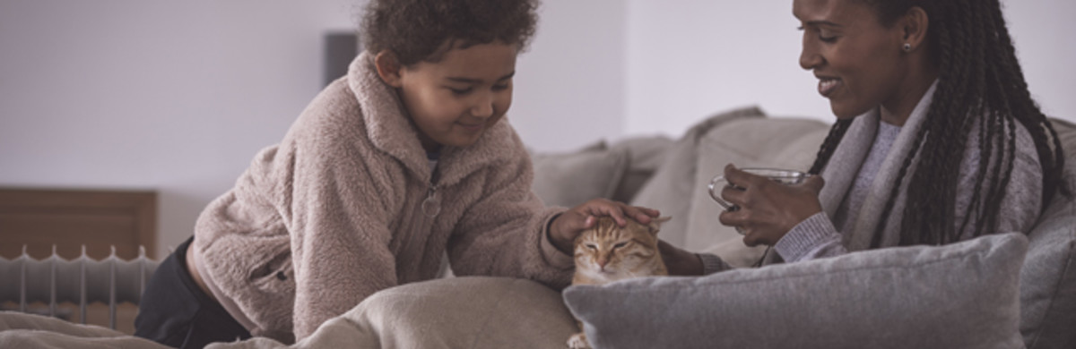 Mother and daughter cosy on a sofa stroking a cute ginger cat